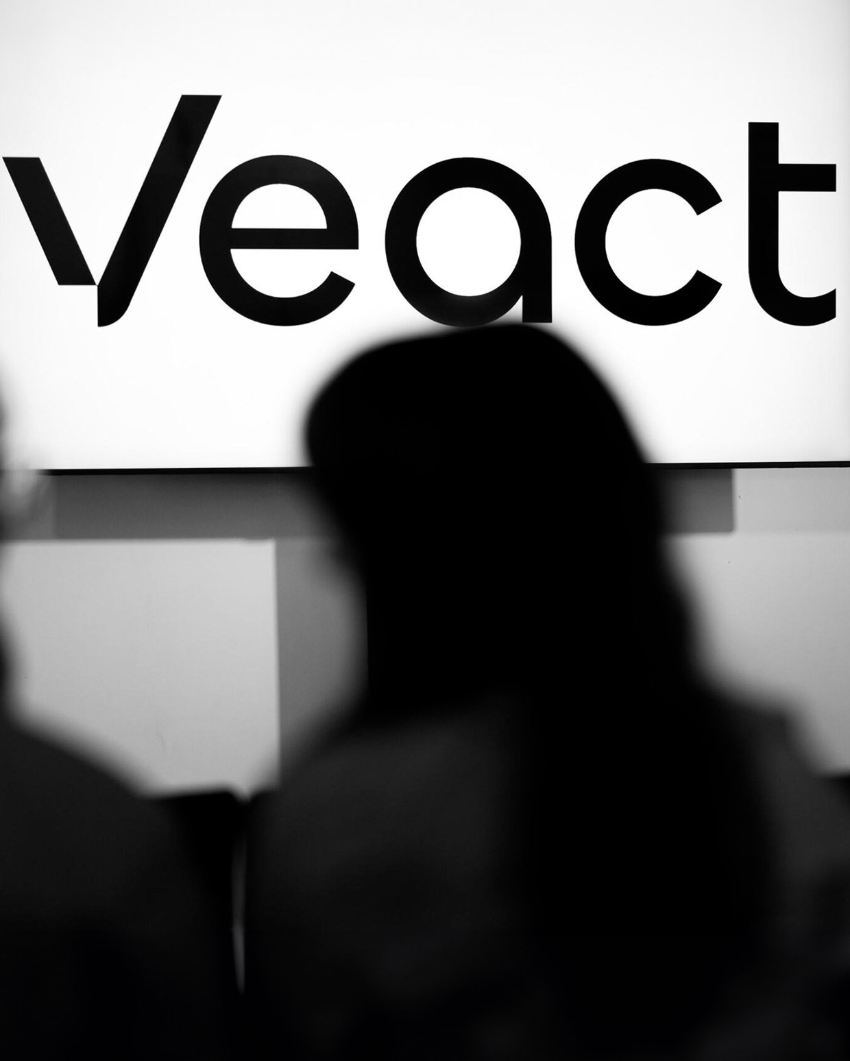 Unscharfes Publikum vor einem Schild mit dem "Veact"-Logo