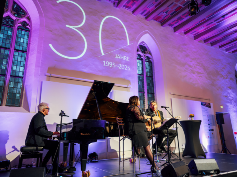 Musiker performen beim IfA Branchengipfel 2025 in festlich beleuchtetem Saal mit Projektion 30 Jahre 1995–2025 im Hintergrund