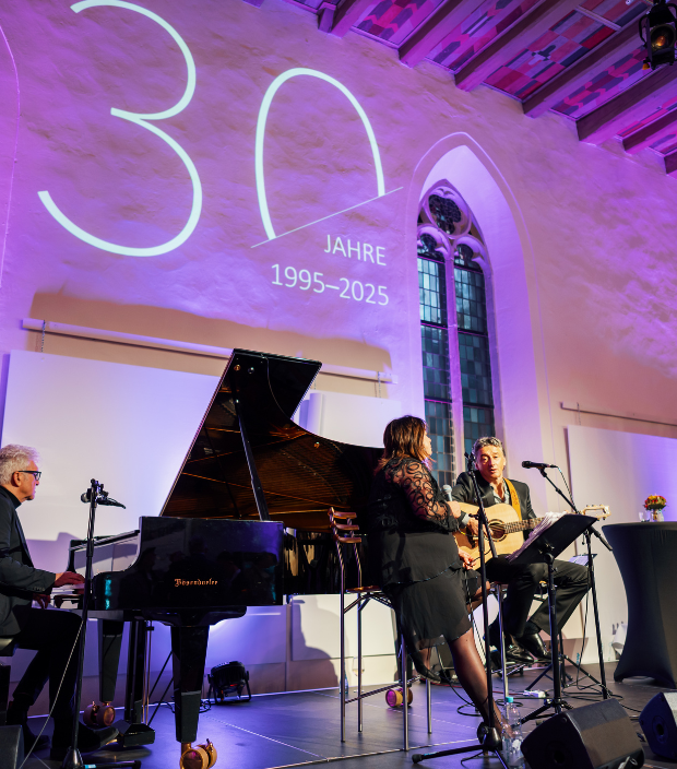 Musiker performen beim IfA Branchengipfel 2025 in festlich beleuchtetem Saal mit Projektion 30 Jahre 1995–2025 im Hintergrund