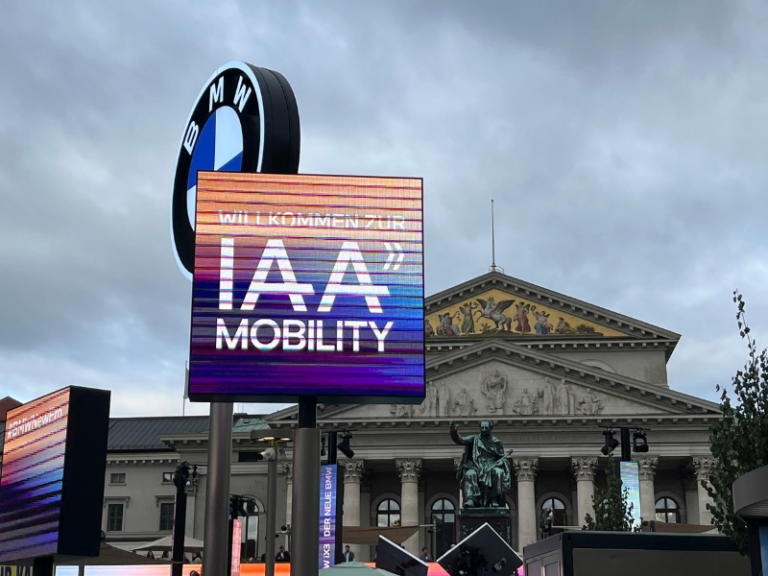 Leuchtendes Willkommensschild der IAA Mobility 2025 in München vor dem Nationaltheater mit BMW Logo im Hintergrund