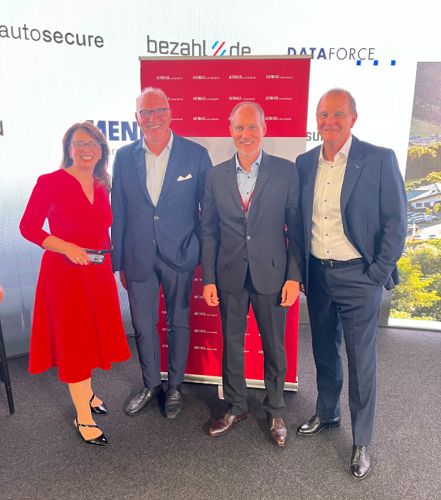 Geschäftsleute auf der AUTOHAUS Sommerakademie 2025 stehen vor einem roten Banner und repräsentieren Innovation und Zusammenarbeit in der Branche