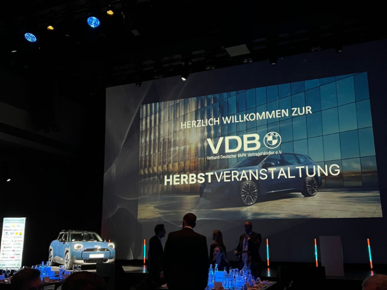 Blick auf die Bühne der VDB Herbstveranstaltung 2025 mit Fahrzeugpräsentation und Teilnehmenden im Veranstaltungsraum