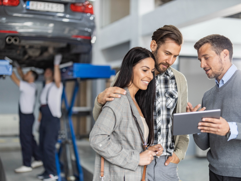 Serviceberater berät Kunden im Autohaus mit Tablet während Werkstattservice im Hintergrund
